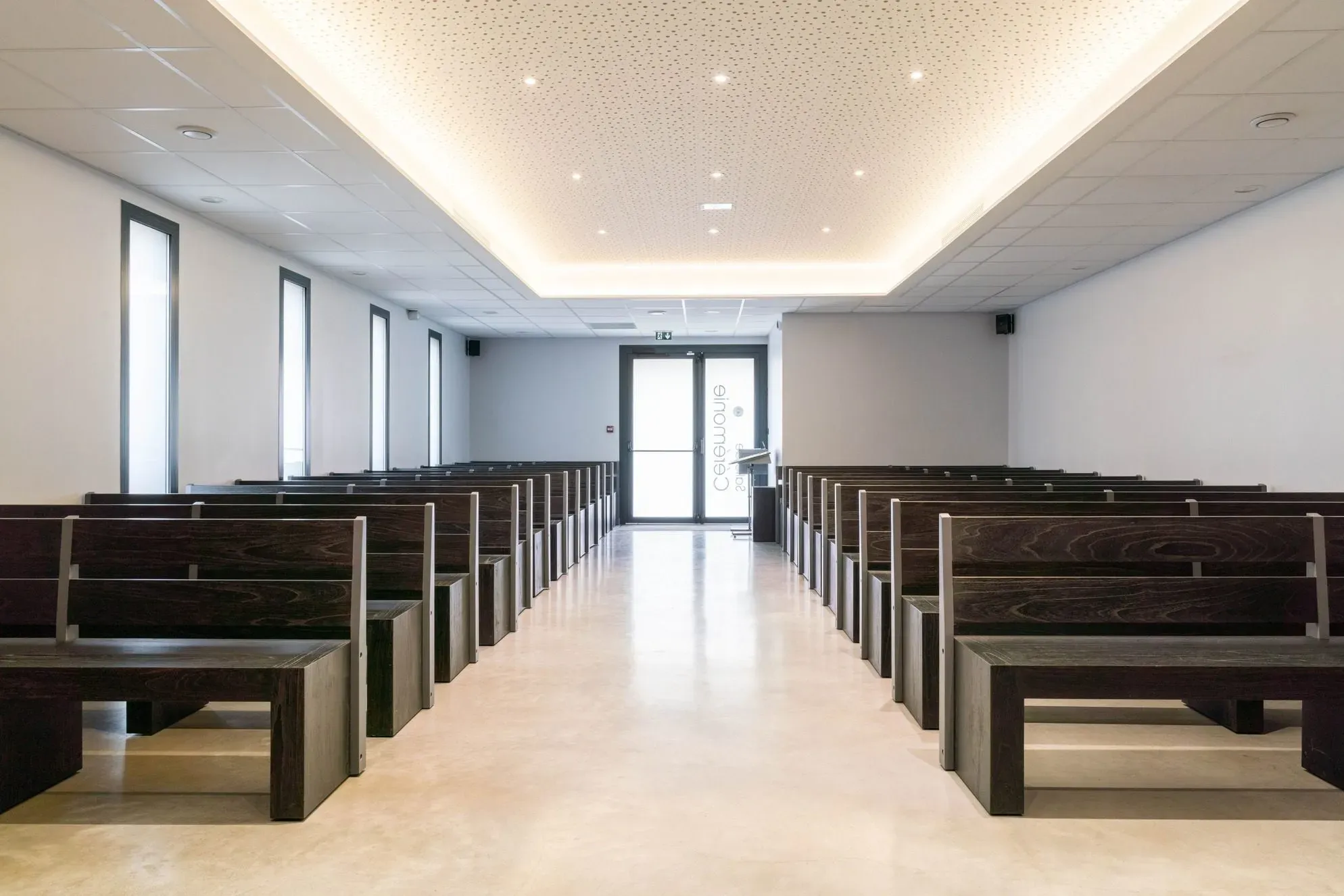 Grande salle de cérémonie funéraire avec bancs en bois sombres alignés.